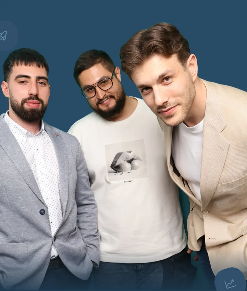 Three young men posing together against a blue background, one leaning forward wearing a beige blazer.