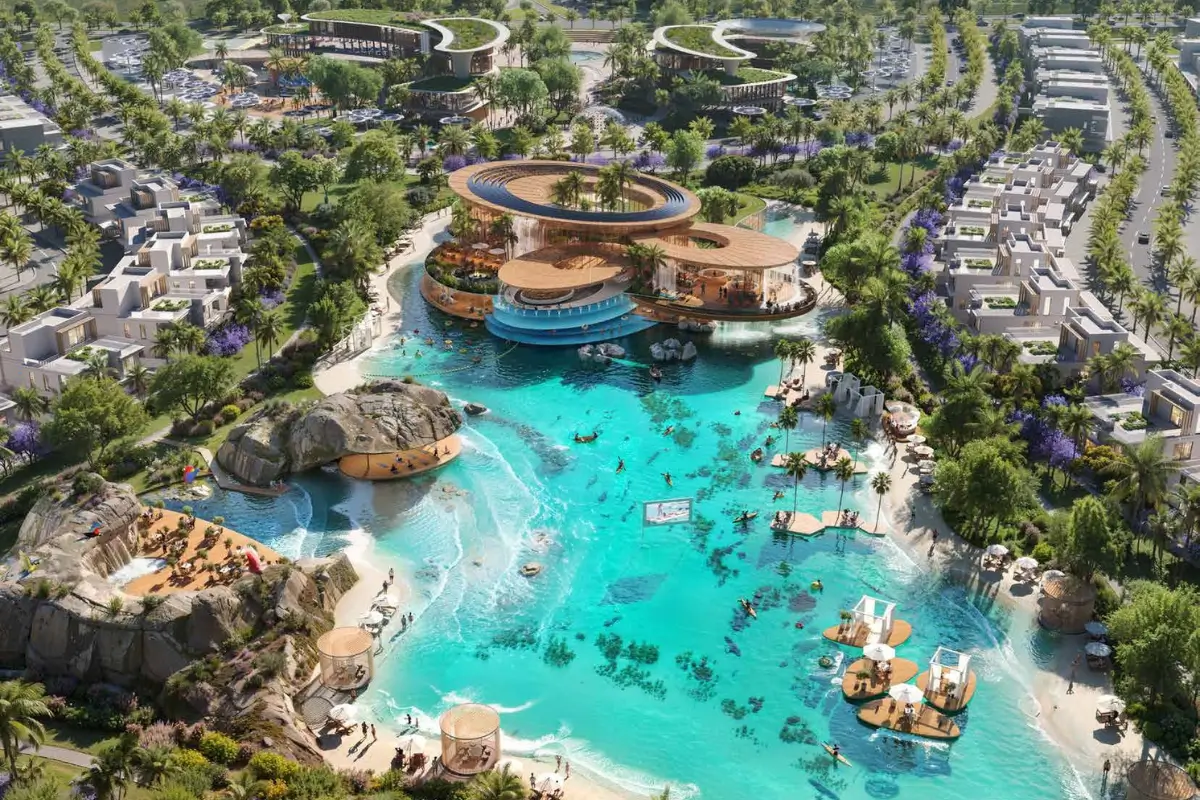Aerial view of a modern resort with turquoise lagoon, circular wooden pavilion, rocky beach, and surrounding villas amidst lush greenery.