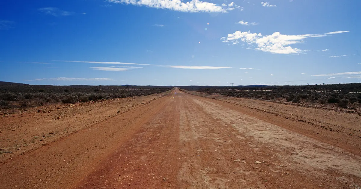 Fill dirt supply shown on a rural red dirt road extending through a barren landscape under a clear blue sky.