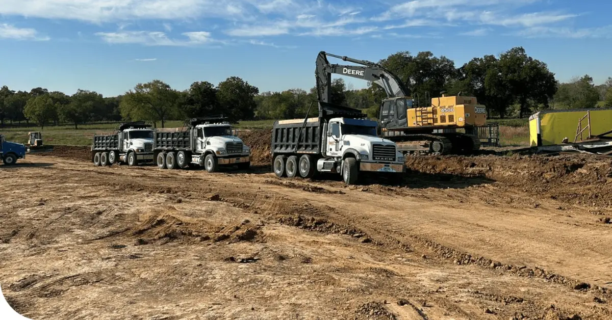 Bulk engineered soil loaded into dump trucks by an excavator at a large open construction site.