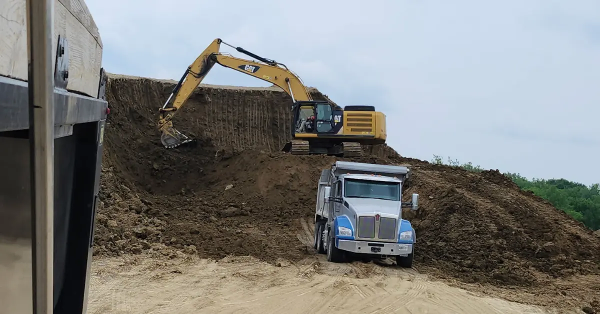 Bulk aggregate being excavated and loaded into a dump truck at a construction site.
