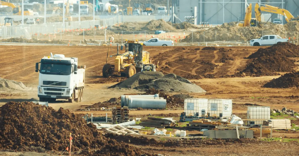 Compacted fill material spread across a large construction area with trucks and graders in operation.