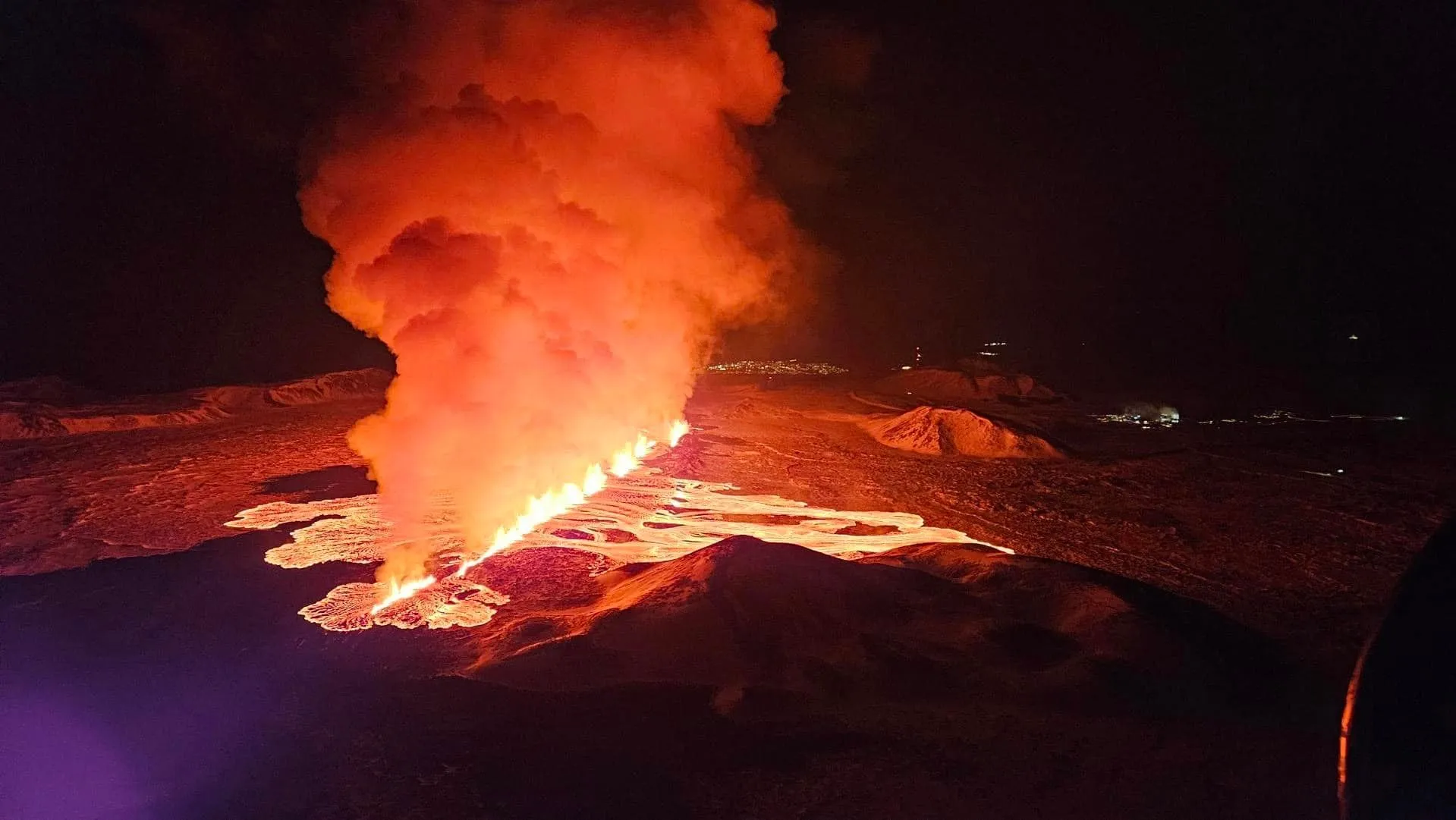 Lava fissure eruption at night on the Reykjanes Peninsula with glowing orange flows across dark basalt field, Iceland