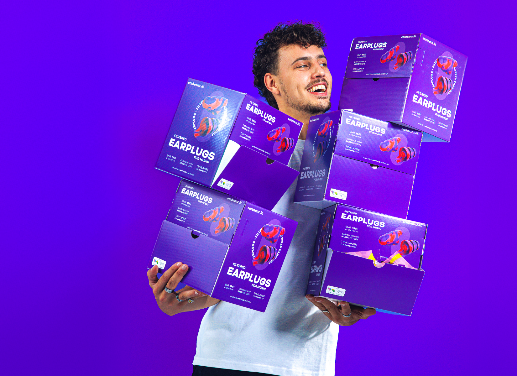 Een lachende jongen die 6 dozen earbeanz vasthoudt.