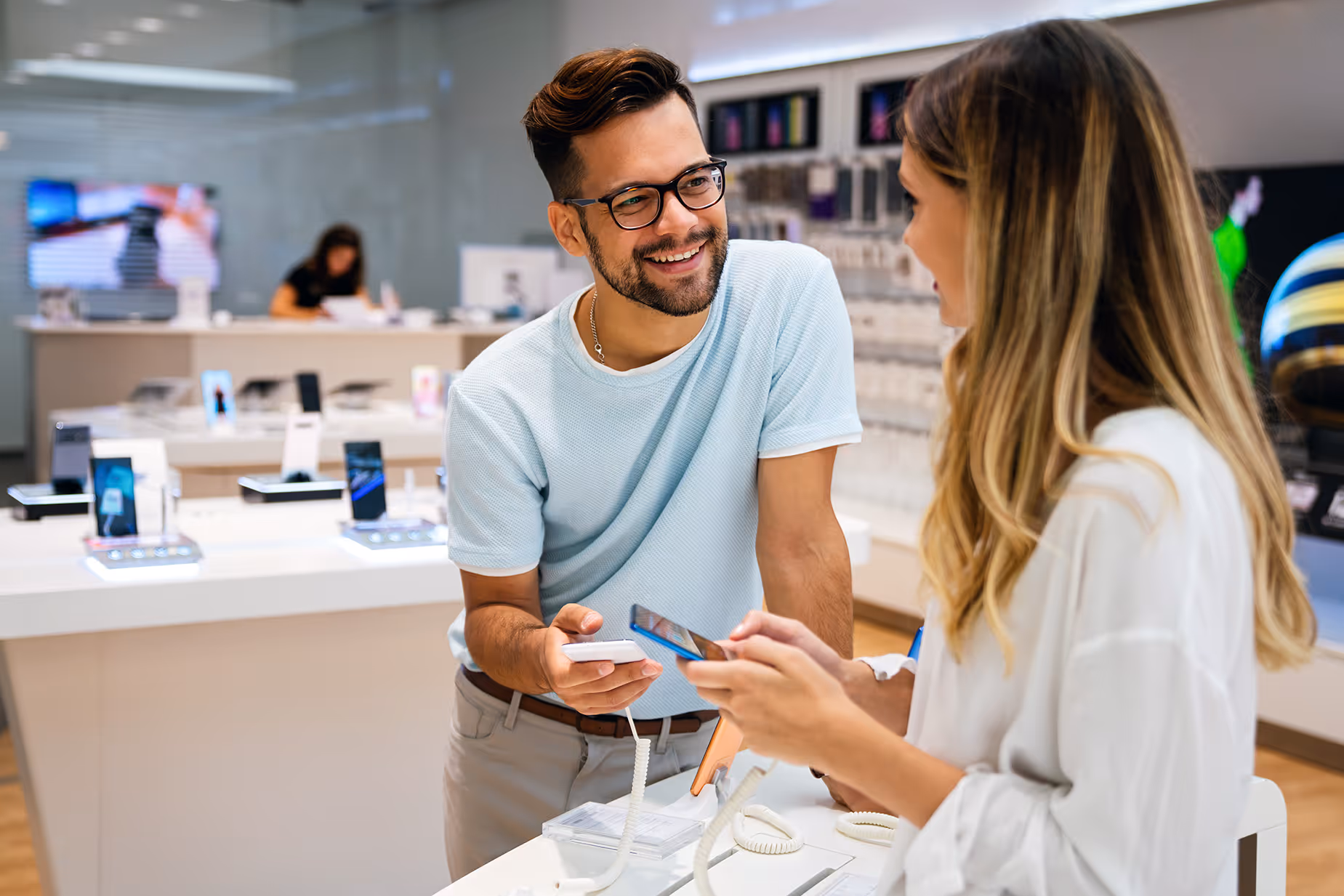 Smiling man and woman interacting while testing smartphones in a modern mobile phone store.