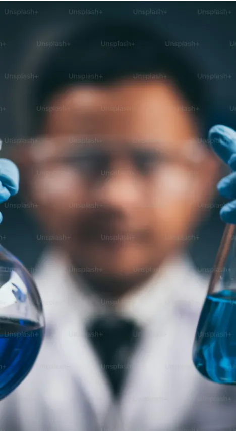 A man in a lab coat holding two flasks filled with blue liquid.