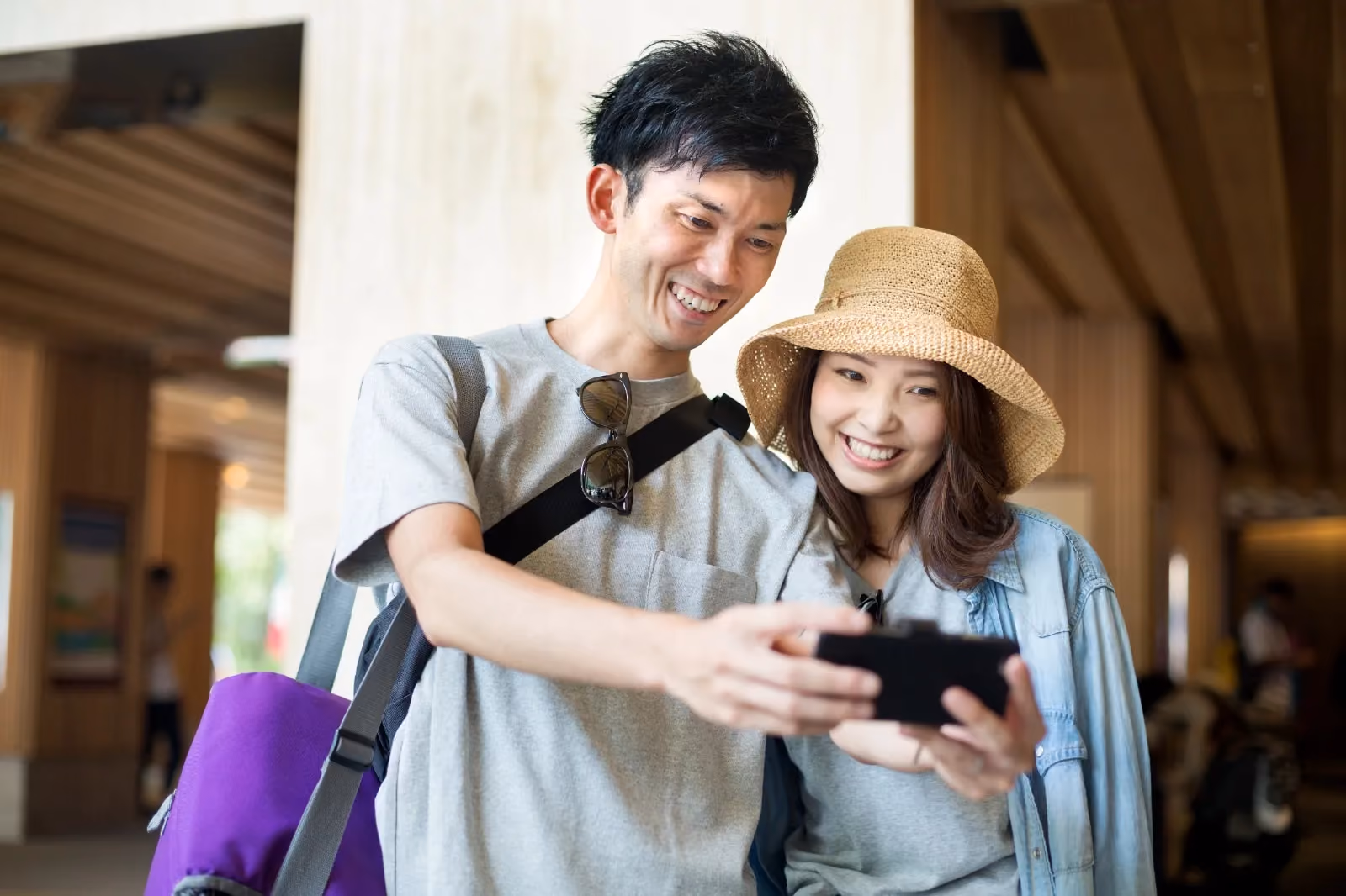 Pasangan wisatawan tersenyum sambil melihat ponsel saat berlibur, menggambarkan kemudahan transaksi digital industri travel dan hospitality dengan DOKU Payment Gateway.