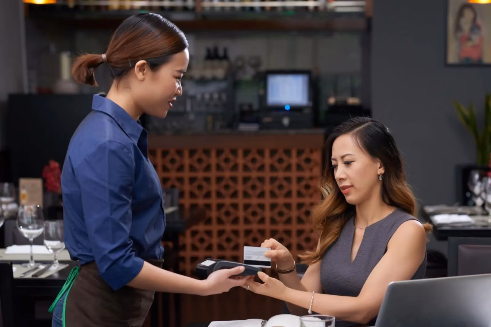 Seorang kasir memproses pembayaran kartu untuk pelanggan di restoran, menggambarkan kemudahan menerima pembayaran tanpa perlu kemampuan teknis.