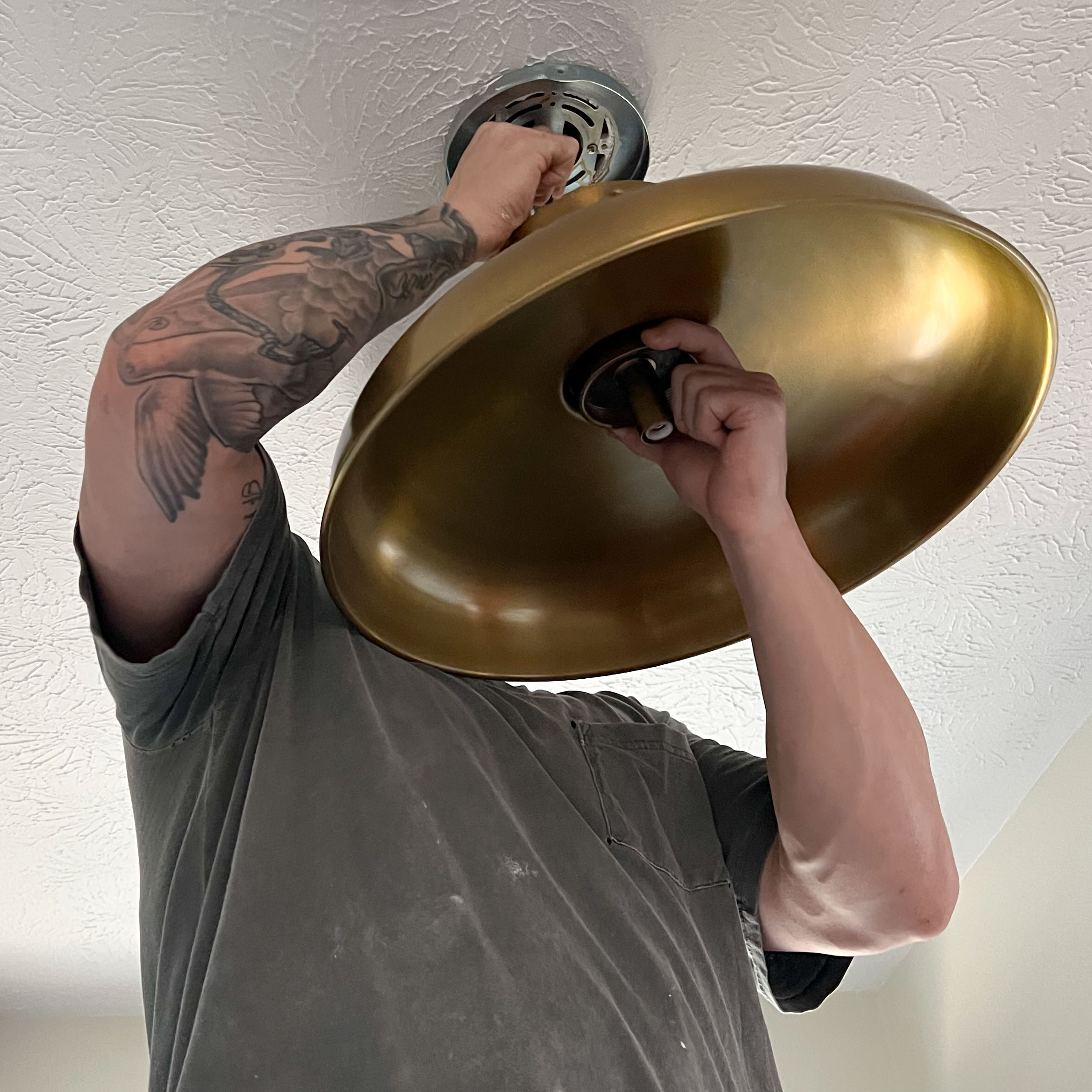 Person installing a large brass ceiling light fixture on a textured white ceiling.