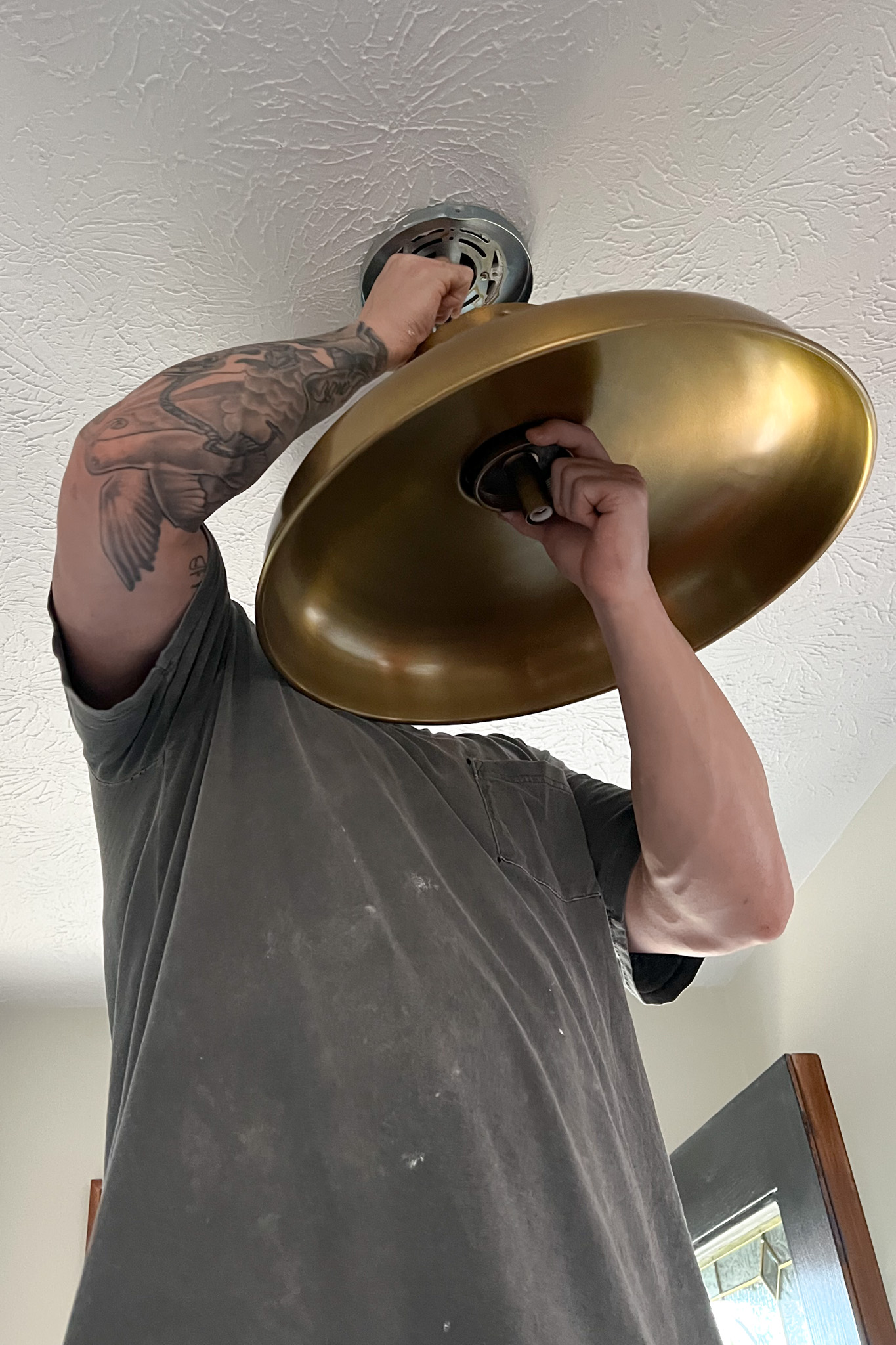 Close up of a man holding up a new brass light fixture and attaching it to the ceiling.