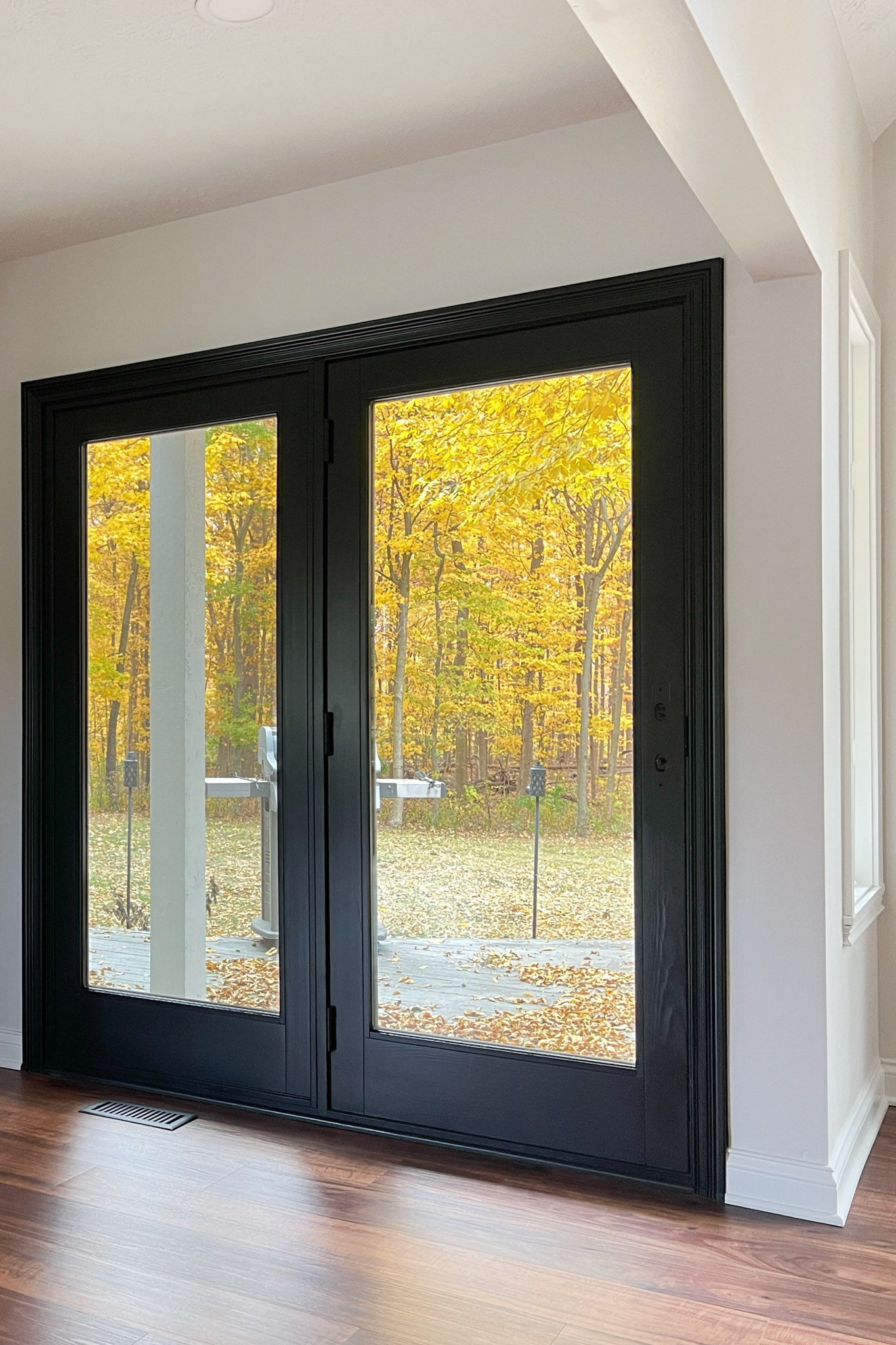 Close-up of black French doors showcasing a vibrant yellow and orange fall scene outdoors.