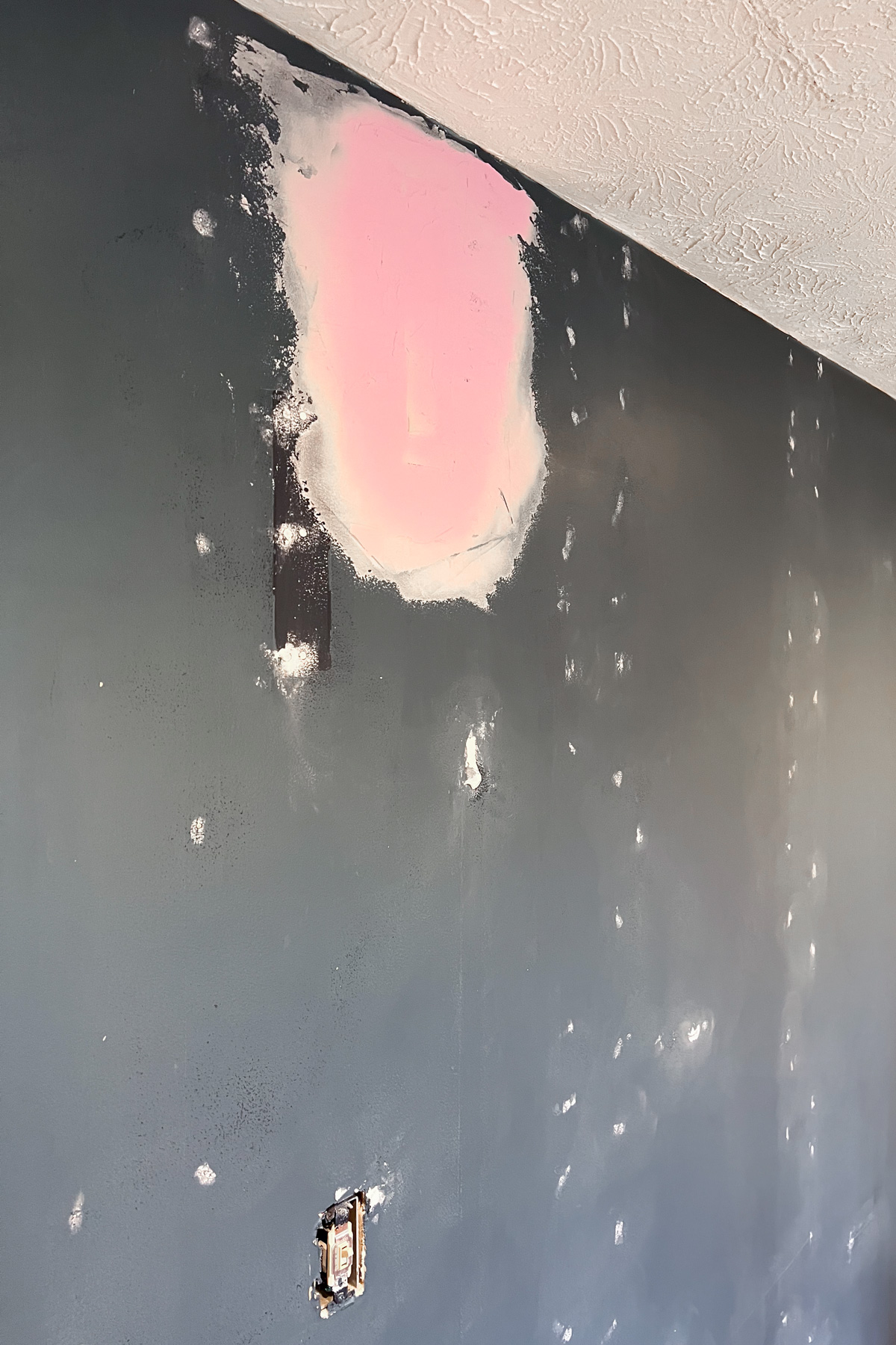 A navy blue wall featuring multiple small white spackle spots and one large patch of pink color-changing joint compound near the ceiling.