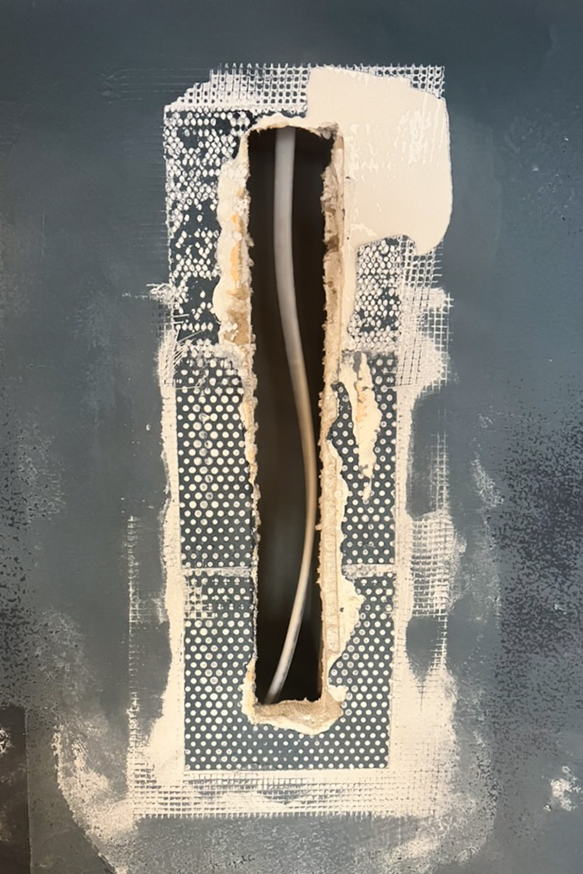 A close-up of a rectangular hole in a wall showing internal wiring, surrounded by mesh tape and a partial application of white joint compound.