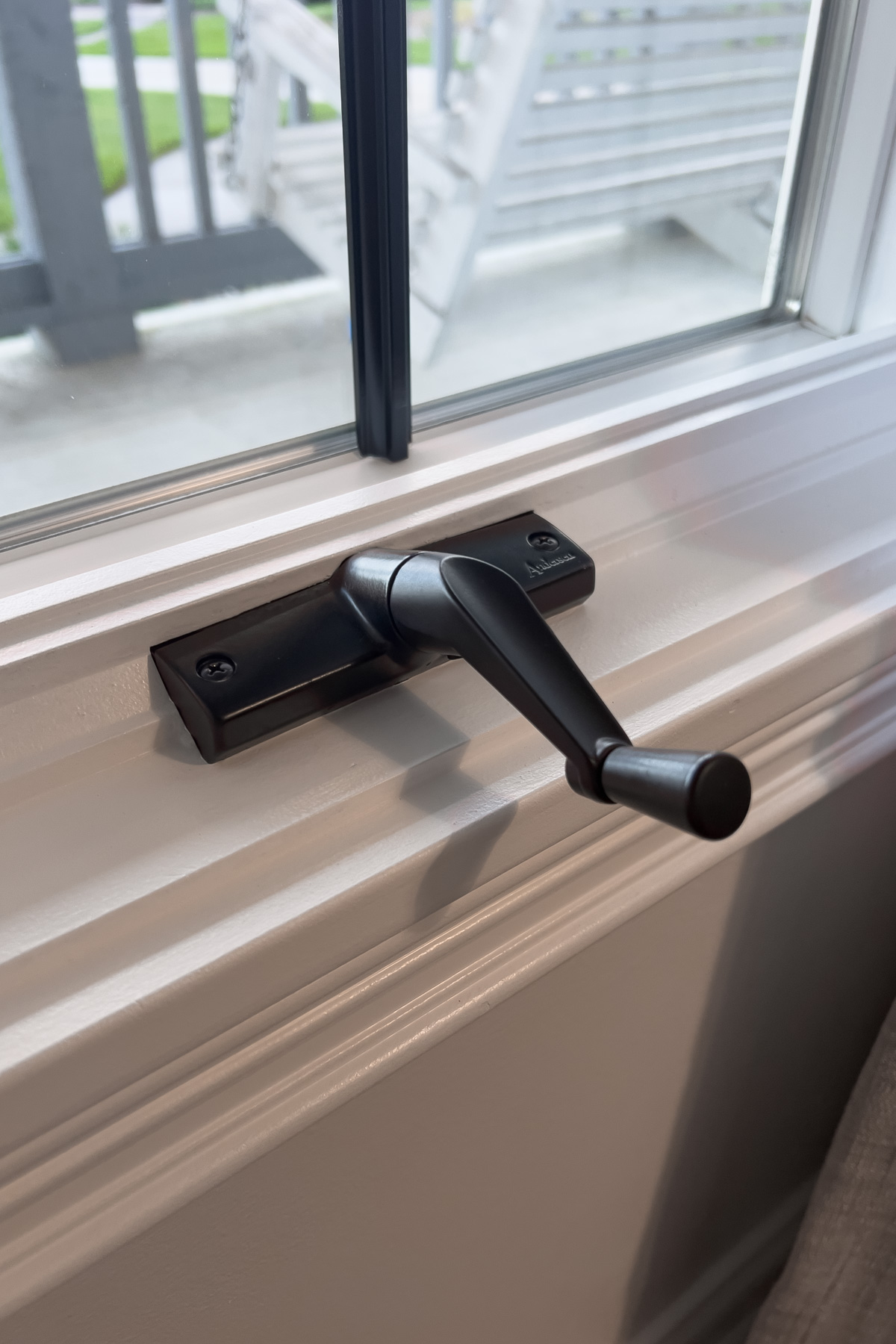 Close-up of a matte black hand-crank installed on a white window sill.