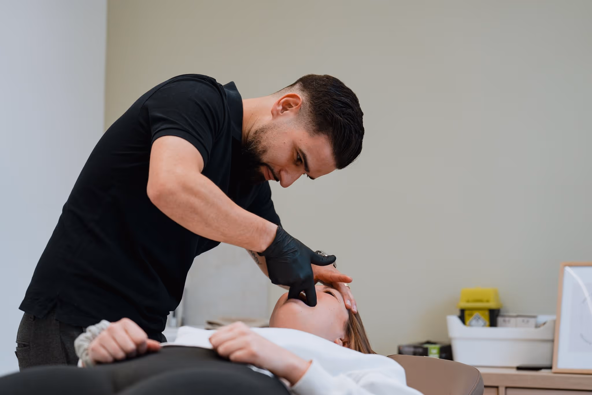 Man wearing black gloves examining a woman's mouth while she lies on a medical chair.