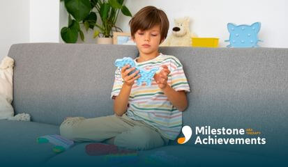 A young child sits comfortably on a couch, deeply engaged & focused while playing with a bright, colorful pop-it sensory toy.