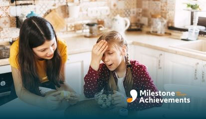 Two autistic girls in the kitchen, one is looking frustrated, while the other is showing her a container.