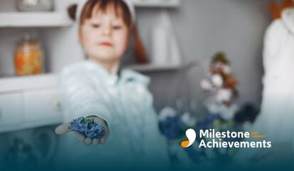 A young autistic girl holding out a small bunch of flowers, offering them with a smile after ABA therapy.