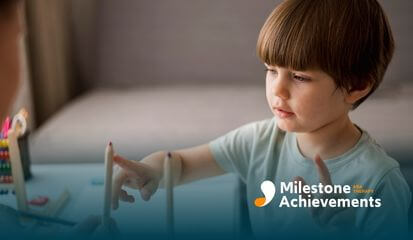 A autistic young boy pointing at a red and blue colored pencil during ABA therapy and learning activity.