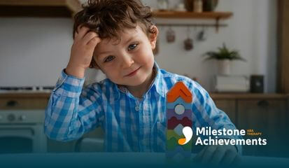 A autistic boy smiling while placing blocks in a stack, showing a playful and joyful expression after ABA therapy.
