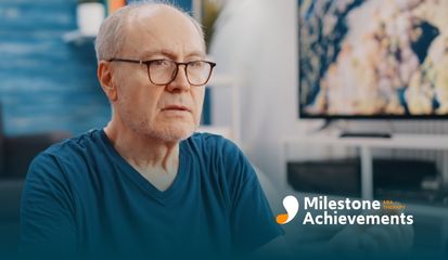 A senior man wearing glasses sits comfortably, using expressive hand gestures while engaging in a lively conversation.