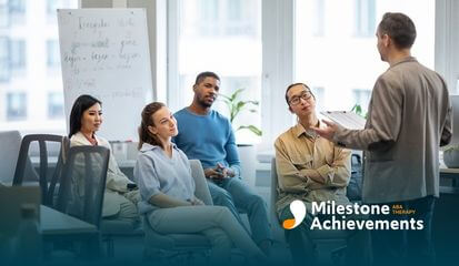 The ABA therapist is leading a discussion with four people listening attentively in an office space.