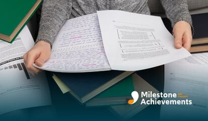 A person is sitting on a couch, holding various documents and notebooks, seemingly in a study session.