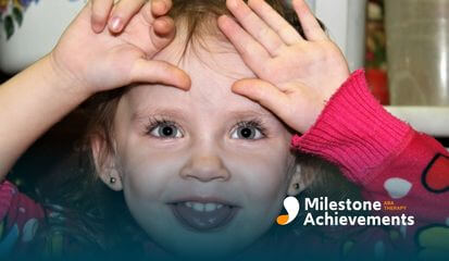 Young child smiling with hands on forehead, expressive facial gesture often associated with play, emotion, or sensory expression