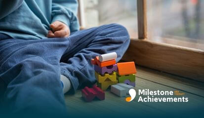 Autistic young boy sitting by a window stacking colorful wooden blocks on the floor, focused on play.