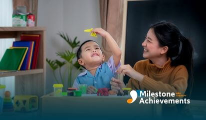 Therapist smiling as a young autistic child plays with colorful modeling clay at a table during ABA therapy 
