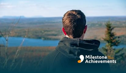 Person seen from behind stands overlooking a wide valley and river, wearing a dark hoodie and viewing a calm landscape.
