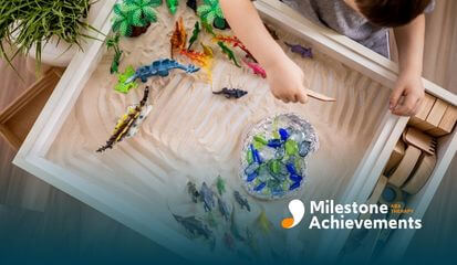 Child explores a sensory table with sand, dinosaur figures, and tools, supporting sensory play and imaginative learning.