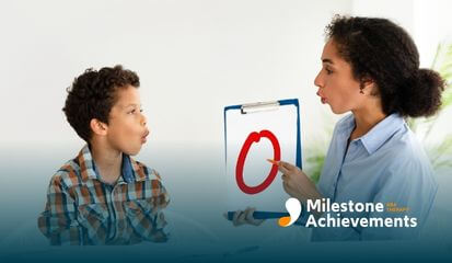 ABA therapist helps a child practice speech sounds by modeling mouth movements and pointing to a visual cue on a clipboard.