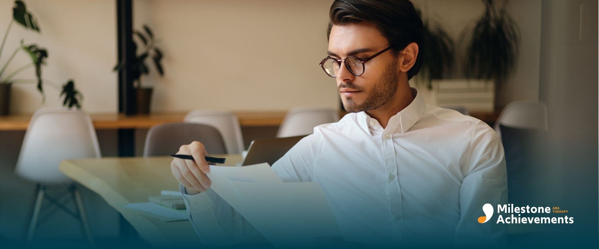 A male therapist in glasses is reviewing a document at a modern office, focused and professional in a quiet work environment.