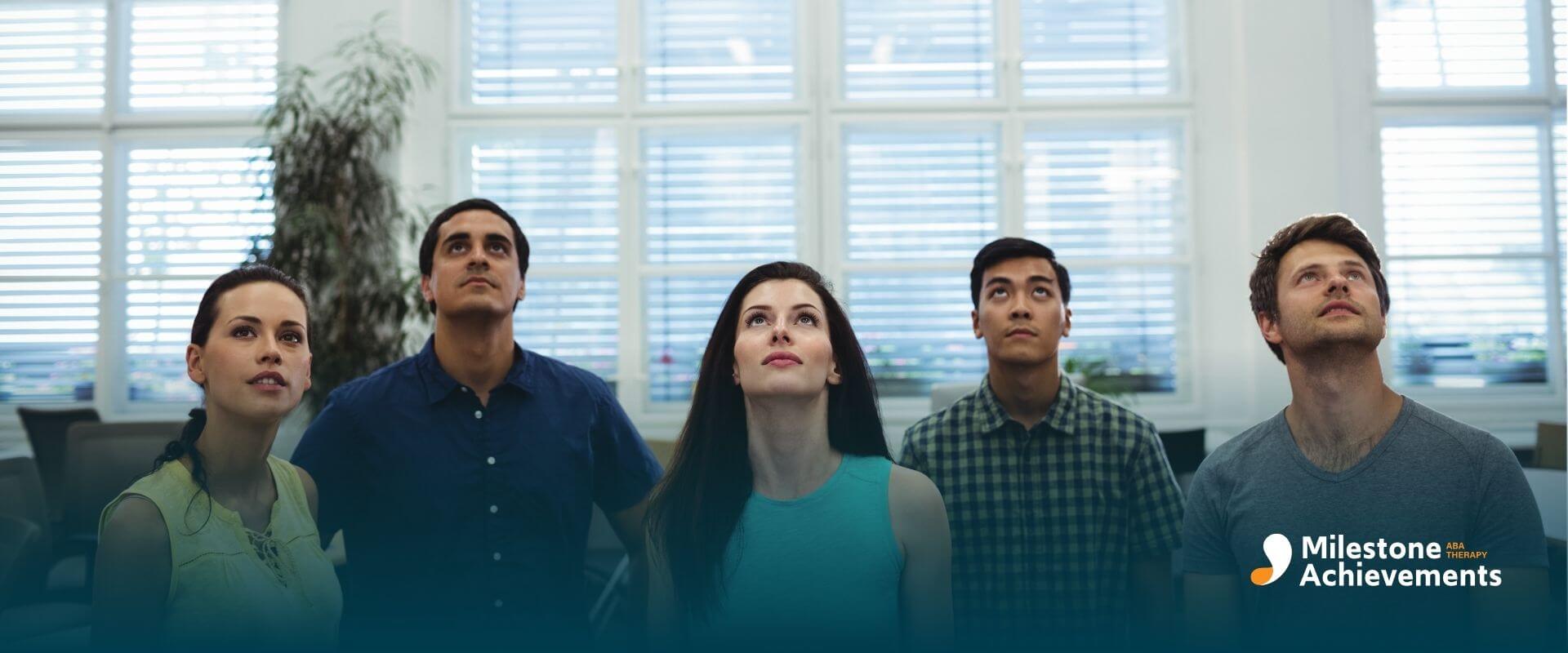 Group of therapists standing in a classroom, looking upward as if listening to instructions or watching a presentation.