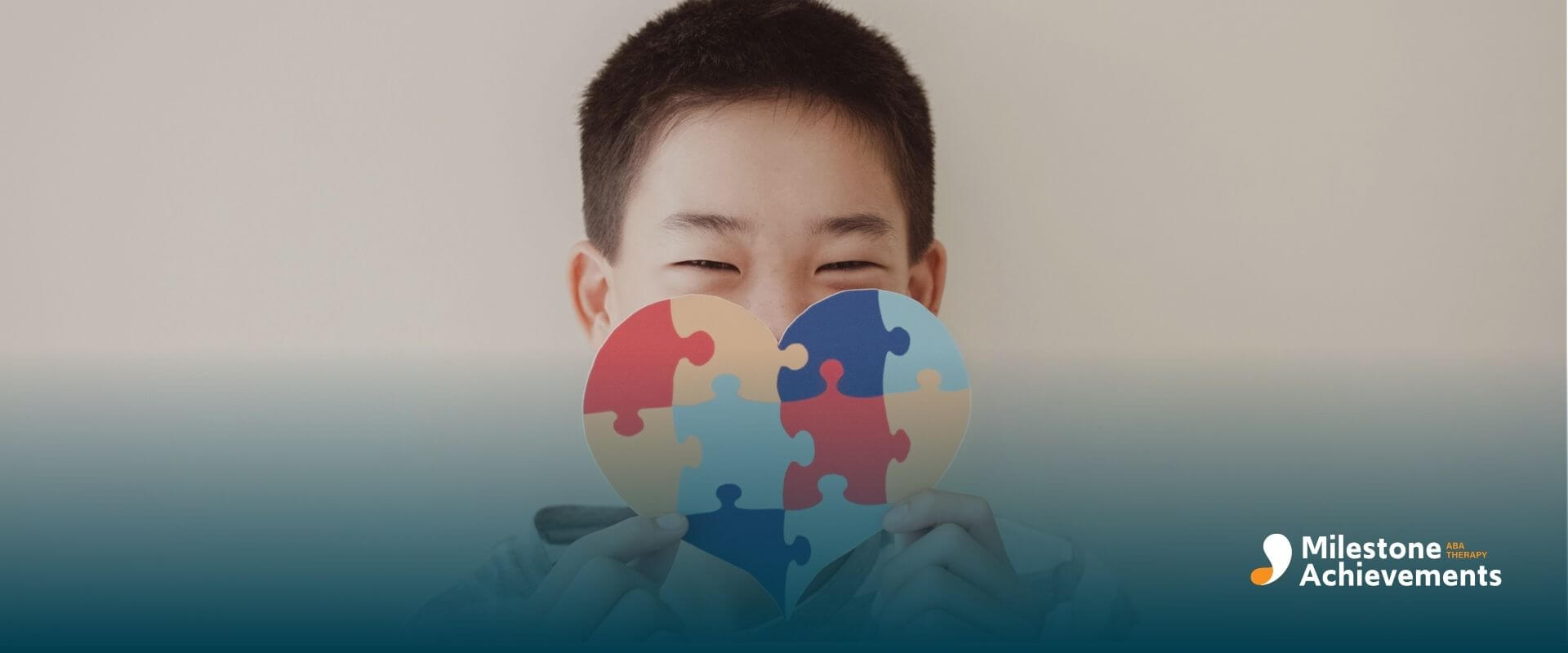 Autistic boy holding a colorful puzzle-piece heart in front of their face, symbolizing autism awareness.