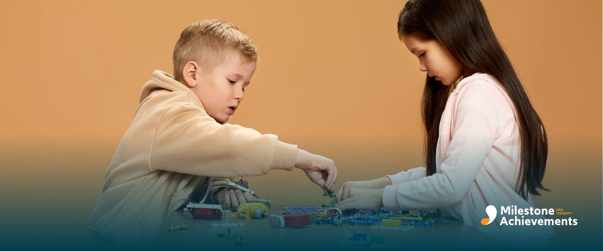 Two autistic children at a table assembling electronic toy parts, showing cooperative play and problem-solving skills.