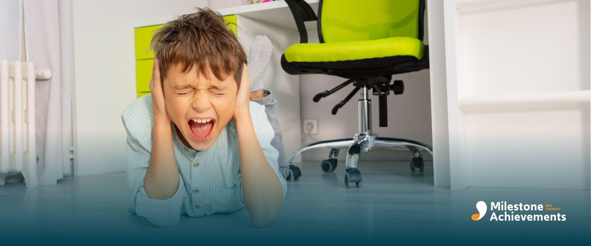 Autistic boy lying on floor covering ears near bright shapes, showing sensory overload and distress in home learning.