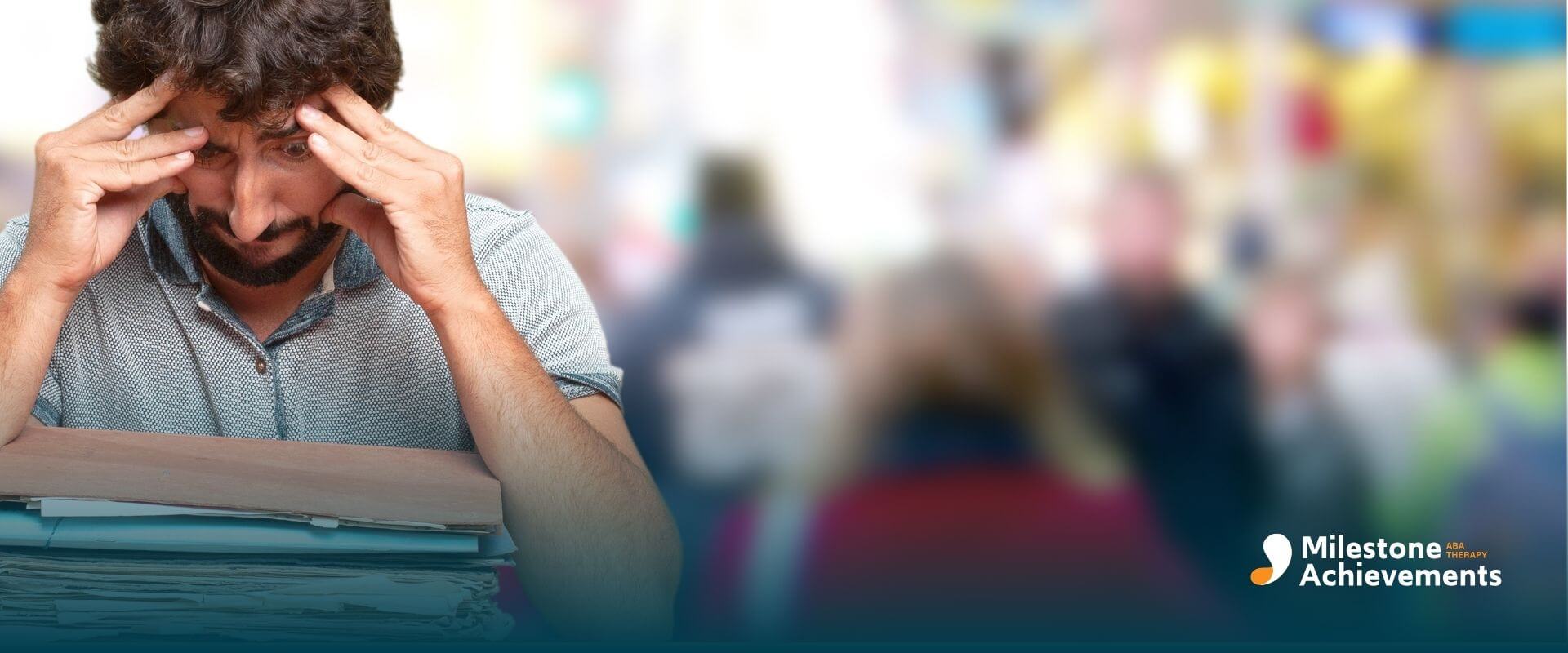 A male therapist holding his head over a large stack of paperwork, symbolizing stress after failing an important exam.
