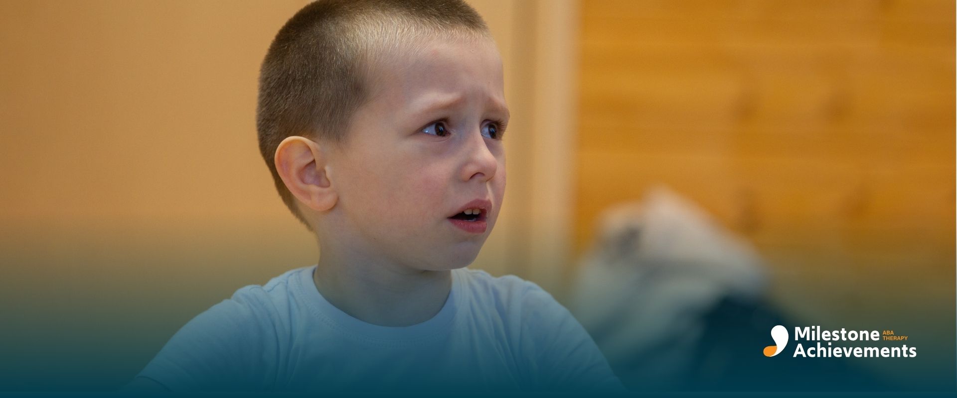 Young autistic child holding a toy with a concerned expression, reacting to something off camera indoors.