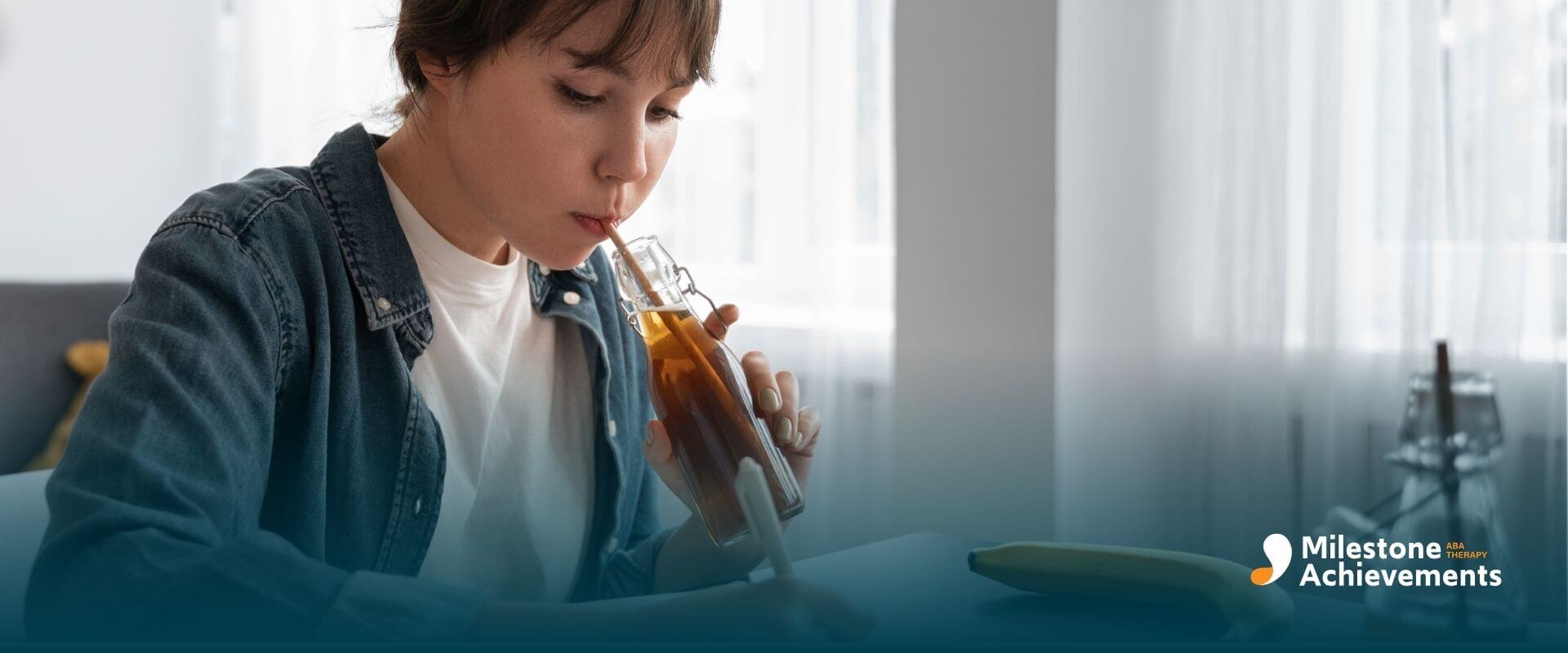 ABA student sitting at a desk drinking from a bottle while writing notes in a notebook during focused study time at home.