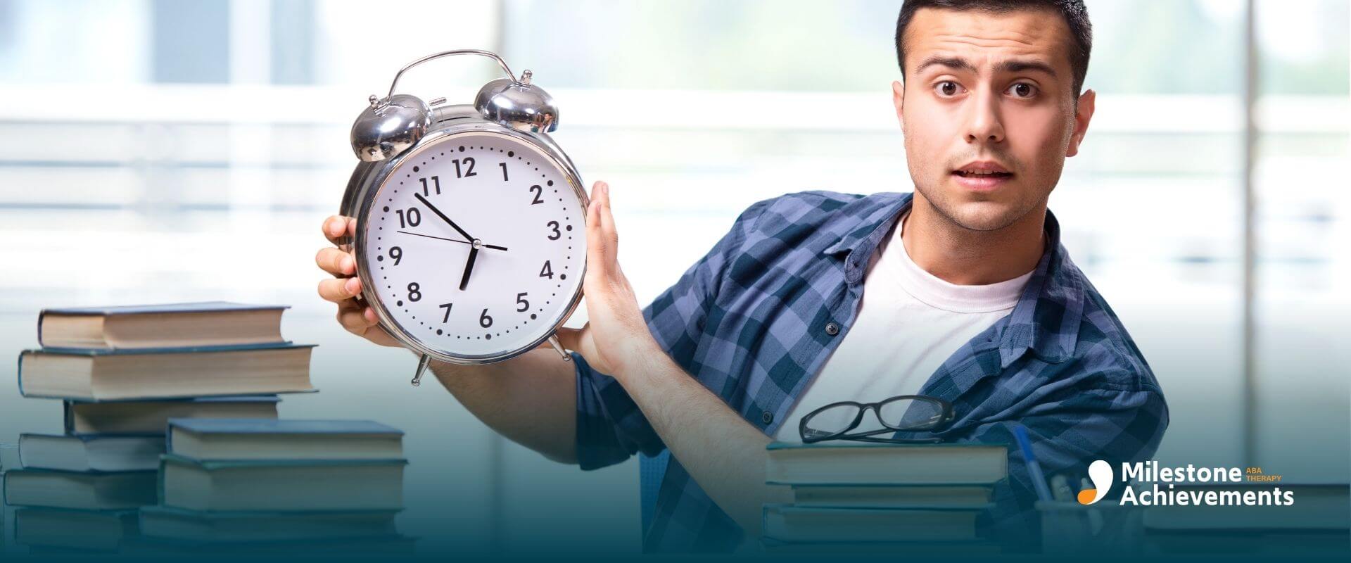 ABA student holding a large alarm clock while sitting at a desk with books, representing time management and study planning.