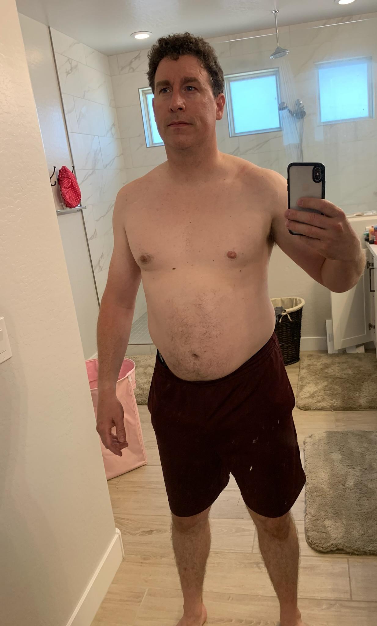 Man with big belly posing int he mirror holding a phone camera