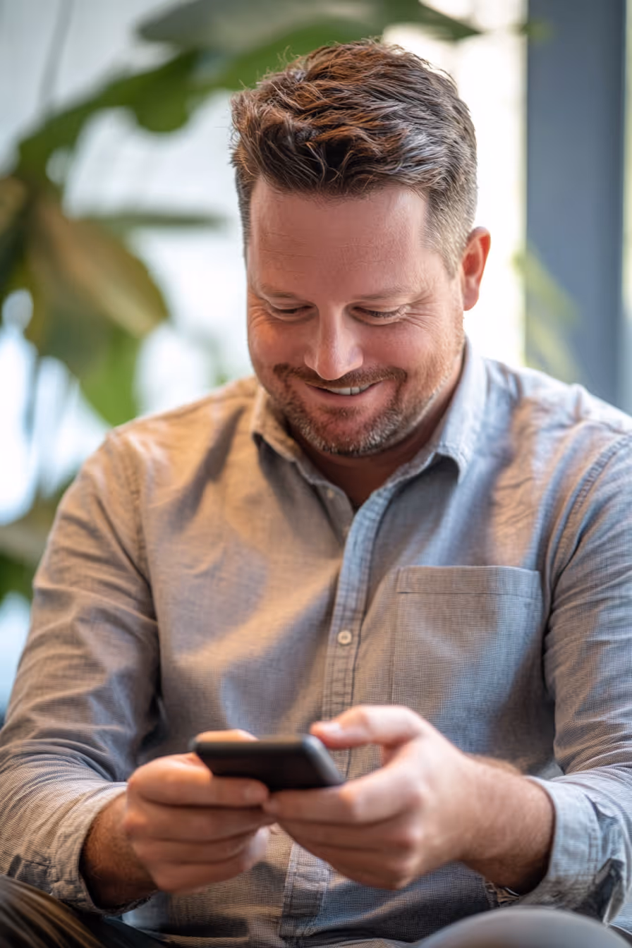 A young man smiling and checking his phone with visible excitement — the moment an employer reaches out after discovering his GoHeadHunt profile.