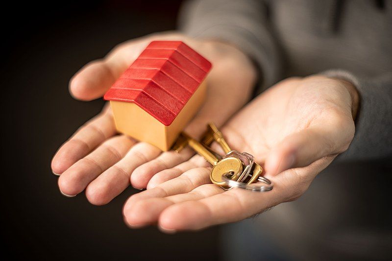 Miniature house and normal sized keys in open hands