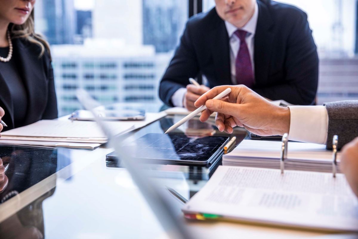 People dressed in suits sitting at a business table speaking over documents