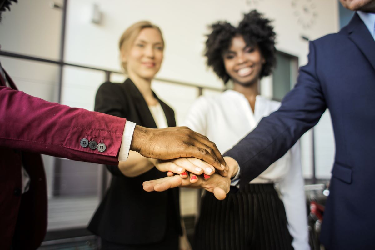 Four young people in business wear placing hands over each other's in a stack