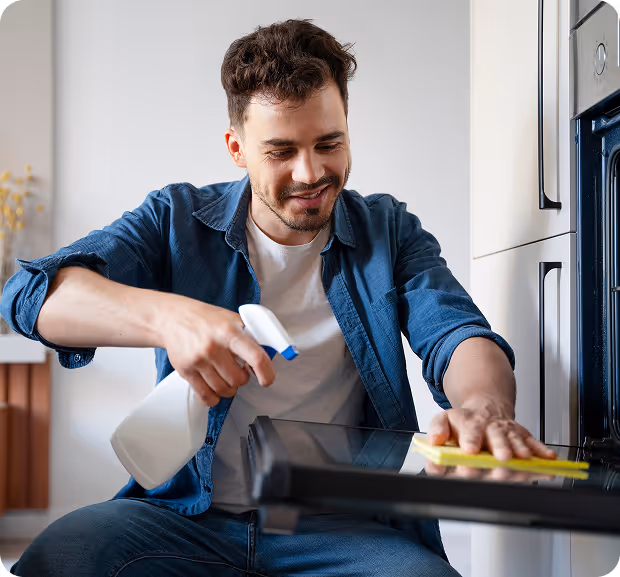 A man scrubs the interior of his oven with a sponge, focusing on removing grease and stains.