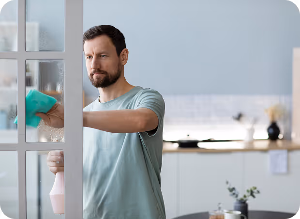 A man is vacuuming a tidy living room, focusing on the carpet while surrounded by furniture and decor.