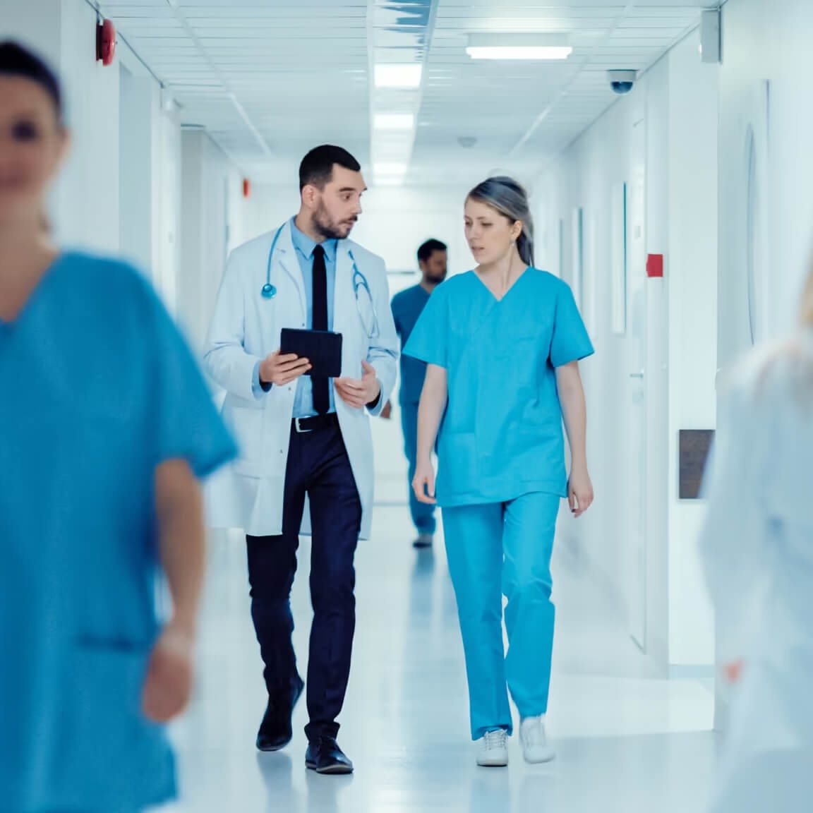 A doctor and a nurse walking through a healthcare facility hallway discussing.